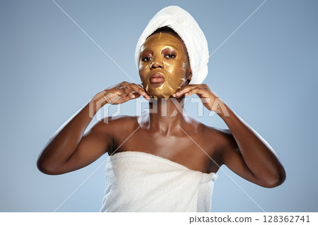 Woman applies gold facial mask while wrapped in a towel in a serene indoor setting 128362741