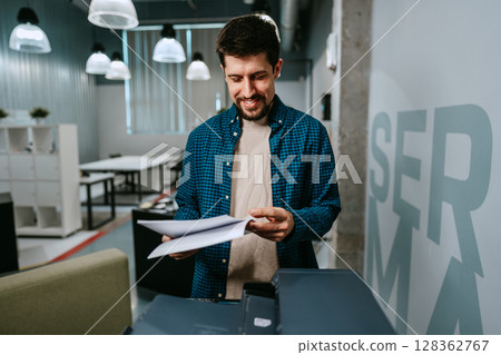 Office worker reviewing printed documents in modern workspace while smiling during a productive day Office worker reviewing printed documents in modern workspace while smiling during a productive day 128362767
