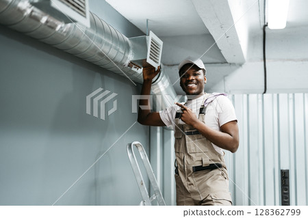 Skilled worker proudly points at air vent in modern workshop during installation process 128362799