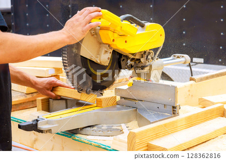 Carpenter person expertly uses miter saw to cut wooden boards under works day 128362816