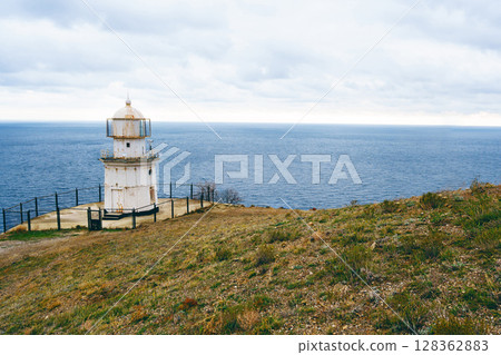 Lighthouse stands on a rugged coastline overlooking the vast ocean under a cloudy sky 128362883