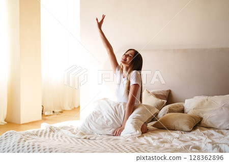 Morning routine of a woman waking up and stretching in a cozy bedroom with natural light pouring in Morning routine of a woman waking up and stretching in a cozy bedroom with natural light pouring in 128362896