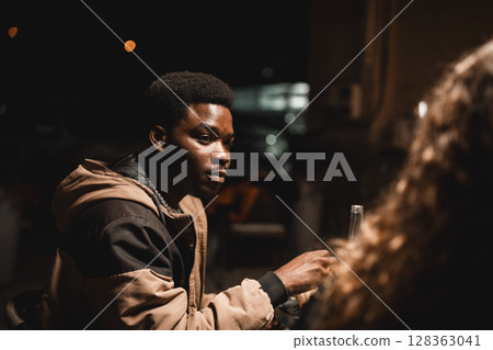 Young man engaged in a deep conversation at a night gathering outside a cafe Young man engaged in a deep conversation at a night gathering outside a cafe 128363041
