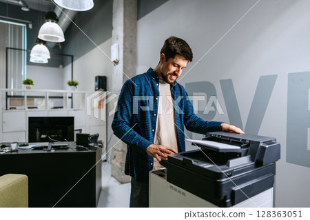 Man operating a printer in a modern office environment during daylight hours 128363051