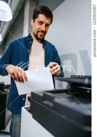 Man operates printer in modern office space while preparing printed documents for work tasks Man operates printer in modern office space while preparing printed documents for work tasks 128363067
