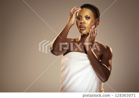 Skincare routine featuring a woman applying a gold mask in a serene indoor setting during early evening Skincare routine featuring a woman applying a gold mask in a serene indoor setting during early evening 128363071