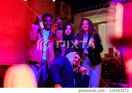 Group of friends celebrating with drinks in a vibrant indoor location during evening hours 128363072