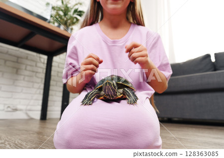 Child sits on floor with turtle on lap while playing at home in cozy living room setting during the afternoon Child sits on floor with turtle on lap while playing at home in cozy living room setting during the afternoon 128363085
