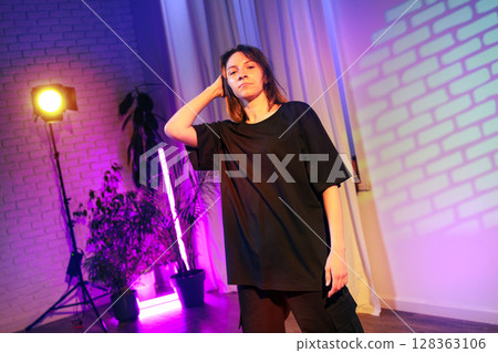 Person posing confidently in a creative space with colorful lighting and plants in the background during an artistic showcase Person posing confidently in a creative space with colorful lighting and plants in the background during an artistic showcase 128363106