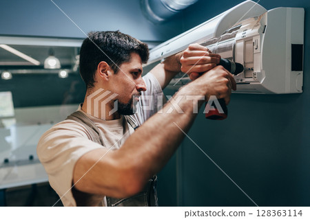 Technician installs air conditioning unit at modern office space during daytime Technician installs air conditioning unit at modern office space during daytime 128363114