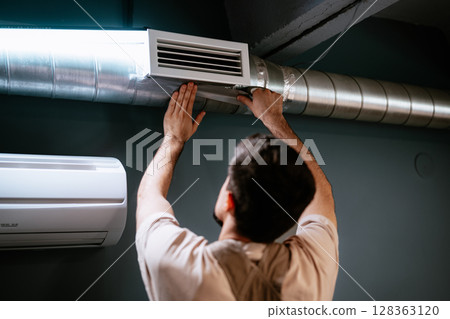 Man servicing air duct in modern interior during home improvement project in the evening 128363120