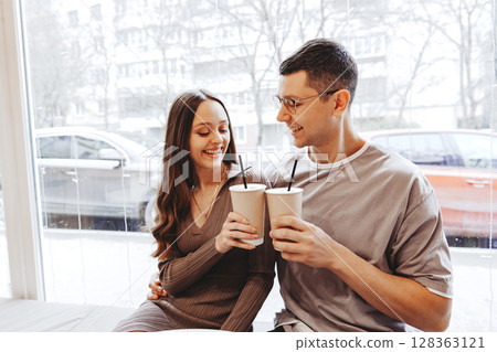 Couple enjoys warm beverages together by the window in a cozy cafe on a winter day 128363121