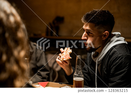 Friends enjoying pizza and drinks in a cozy restaurant during an evening gathering 128363215