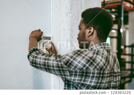 Individual configuring a security system in an industrial workspace during daylight hours Individual configuring a security system in an industrial workspace during daylight hours 128363220