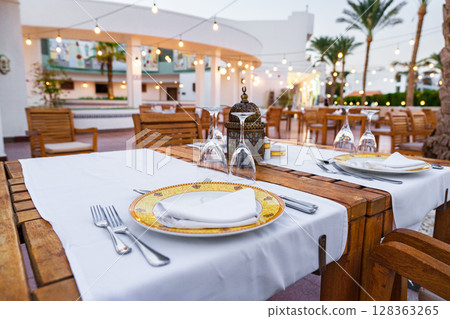 Elegant outdoor dining setup with warm lights and palm trees at a resort restaurant in the evening 128363265