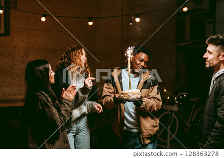 Friends celebrate a birthday outdoors at night with a cake and sparklers while enjoying each other's company Friends celebrate a birthday outdoors at night with a cake and sparklers while enjoying each other's company 128363278