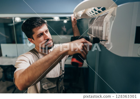 Technician installs air conditioning unit indoors in a modern office setting during the day 128363301