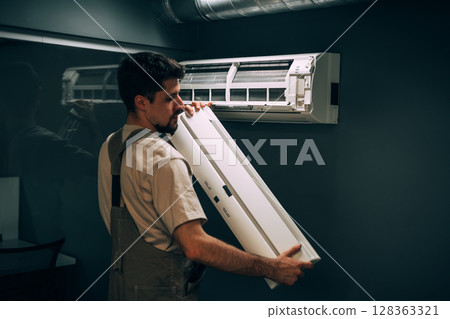 Technician installs air conditioning unit in residential space during the afternoon in a modern indoor setting 128363321