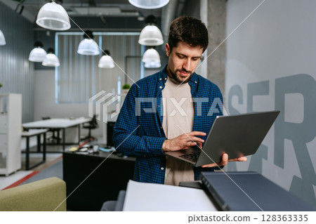 Young man working on laptop in modern office space during daytime Young man working on laptop in modern office space during daytime 128363335