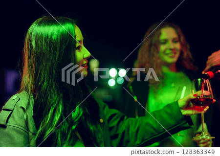 Friends enjoying drinks at a vibrant night gathering with green lighting in a festive atmosphere Friends enjoying drinks at a vibrant night gathering with green lighting in a festive atmosphere 128363349