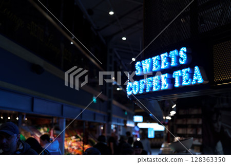 Bright neon sign for coffee and tea shop in bustling market during evening hours Bright neon sign for coffee and tea shop in bustling market during evening hours 128363350