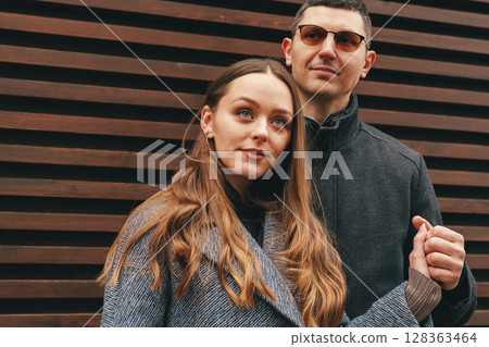 Couple poses together outdoors against a wooden backdrop on a sunny day in an urban setting Couple poses together outdoors against a wooden backdrop on a sunny day in an urban setting 128363464
