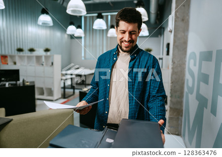 Man smiling while reviewing documents in a modern office setting during daytime Man smiling while reviewing documents in a modern office setting during daytime 128363476