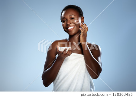 Smiling woman applying skincare product on a clear background during a self-care routine 128363485