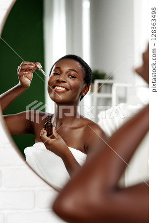 Woman applying skincare serum in a bright bathroom with a modern design during daytime for a glowing complexion Woman applying skincare serum in a bright bathroom with a modern design during daytime for a glowing complexion 128363498