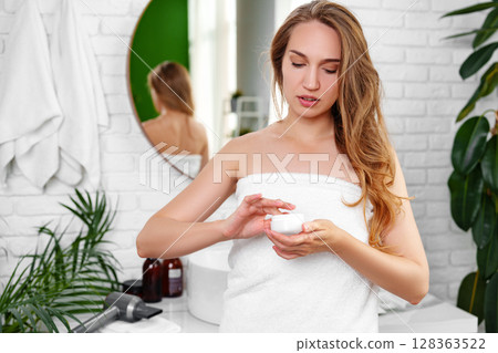 Woman applying cream in a modern bathroom with natural light and greenery during morning routine Woman applying cream in a modern bathroom with natural light and greenery during morning routine 128363522