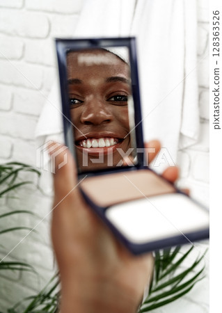 Smiling woman applying makeup in a bright bathroom with plants Smiling woman applying makeup in a bright bathroom with plants 128363526
