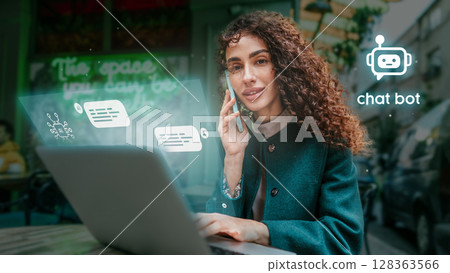 Woman using smartphone while sitting at a cafe table with laptop, engaged in conversation with chat bot technology 128363566
