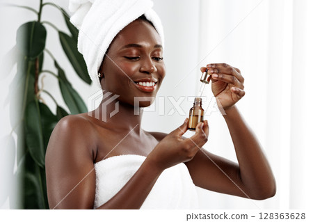 Woman applying skincare serum at home after shower, enjoying self-care routine in bright bathroom 128363628