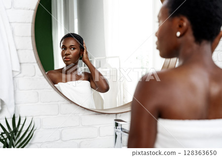 Young woman examines her reflection in a mirror while getting ready in a serene bathroom environment 128363650
