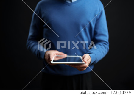 Person using a tablet while standing against a dark background during an indoor setting in a casual environment 128363729