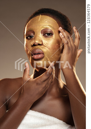 Woman applying a luxurious gold facial mask at a spa during a self-care session 128364579