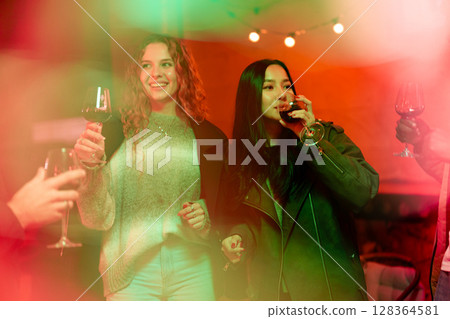 Friends enjoying drinks at a vibrant indoor gathering with festive lighting and cheerful ambiance in the evening Friends enjoying drinks at a vibrant indoor gathering with festive lighting and cheerful ambiance in the evening 128364581