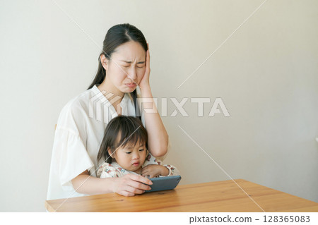 A child looking at a smartphone and a mother with a troubled expression 128365083
