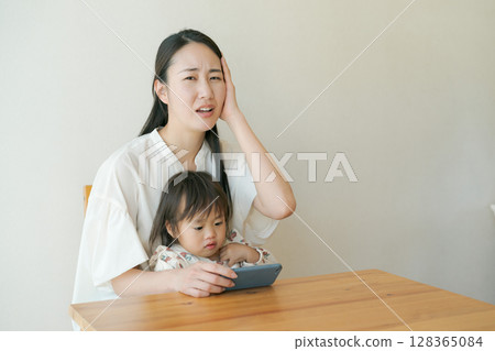 A child looking at a smartphone and a mother with a troubled expression 128365084