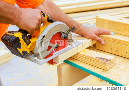 Carpenter cuts lumber using circular saw, craftsmanship careful attention to detail in workshop. 128365148