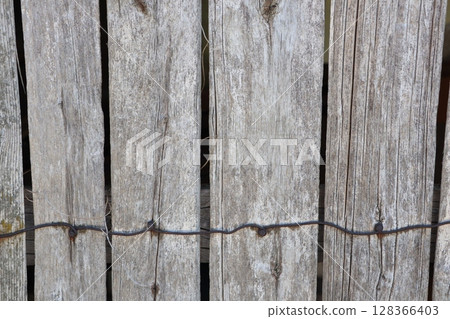 A weathered wooden fence with intricate wire detail, showcasing rustic charm and beauty 128366403