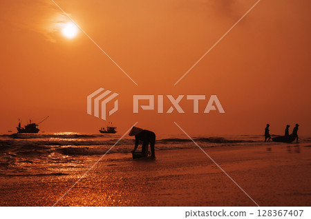 Silhouettes of Vietnamese fishermen with round basket boat and a woman in straw hat in a fishing village in morning at sunrise in Vietnam 128367407