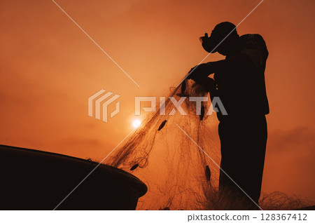 Silhouette of a Vietnamese male fisherman taking out catch of fish from a fishing net in a round boat on beach by the sea in a fishing village in morning at sunrise in Vietnam 128367412