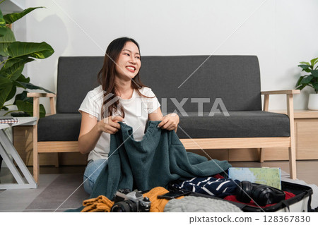 Packing for Travel. Young woman organizing clothes and accessories in a suitcase. 128367830