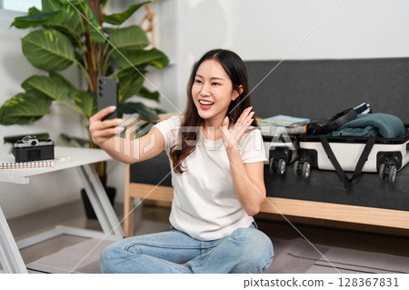 Joyful Travel Preparation. Young woman smiling while taking a selfie during her packing process. 128367831