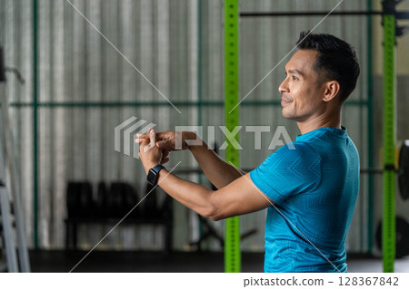 Fitness Stretching Routine. Man performing arm stretches in gym for warm-up. 128367842