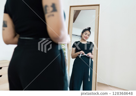 Confident Overweight Woman Measuring Waist in Front of Mirror for Body Positivity and Self-Acceptance 128368648