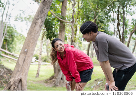 Young Couple Enjoying Outdoor Exercise in a Lush Green Park, Smiling and Staying Hydrated During Their Fitness Routine 128368806