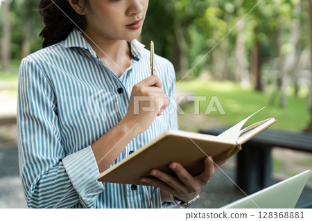 young student studying outdoors, holding a notebook sitting at university park 128368881