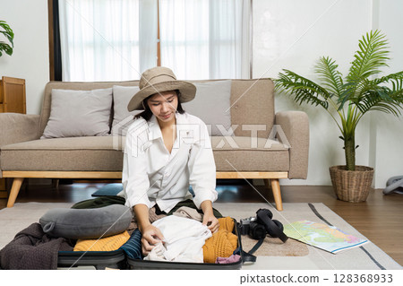 Woman Packing Suitcase for Travel with Clothing and Accessories in Cozy Living Room Setting 128368933
